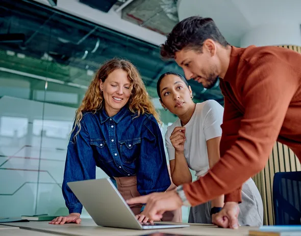Three colleagues gathered around a laptop while one points at the screen