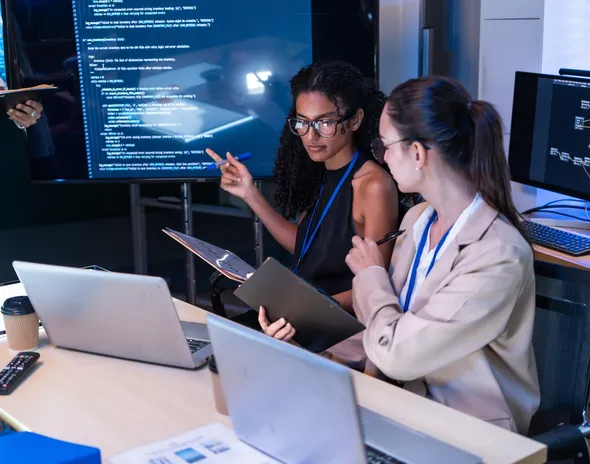 Two colleagues reviewing code on a large wall screen
