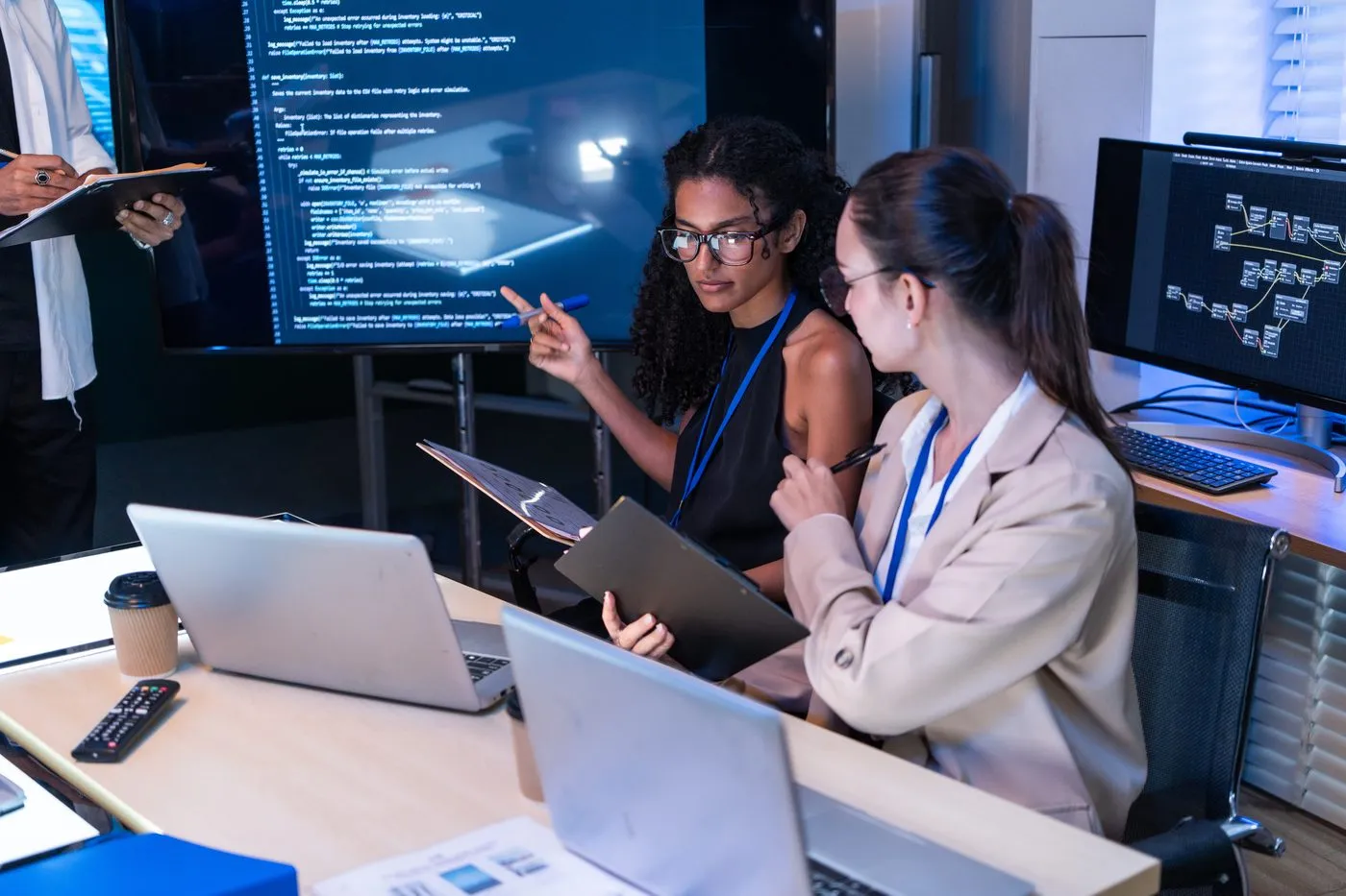 Two colleagues reviewing code on a large wall screen