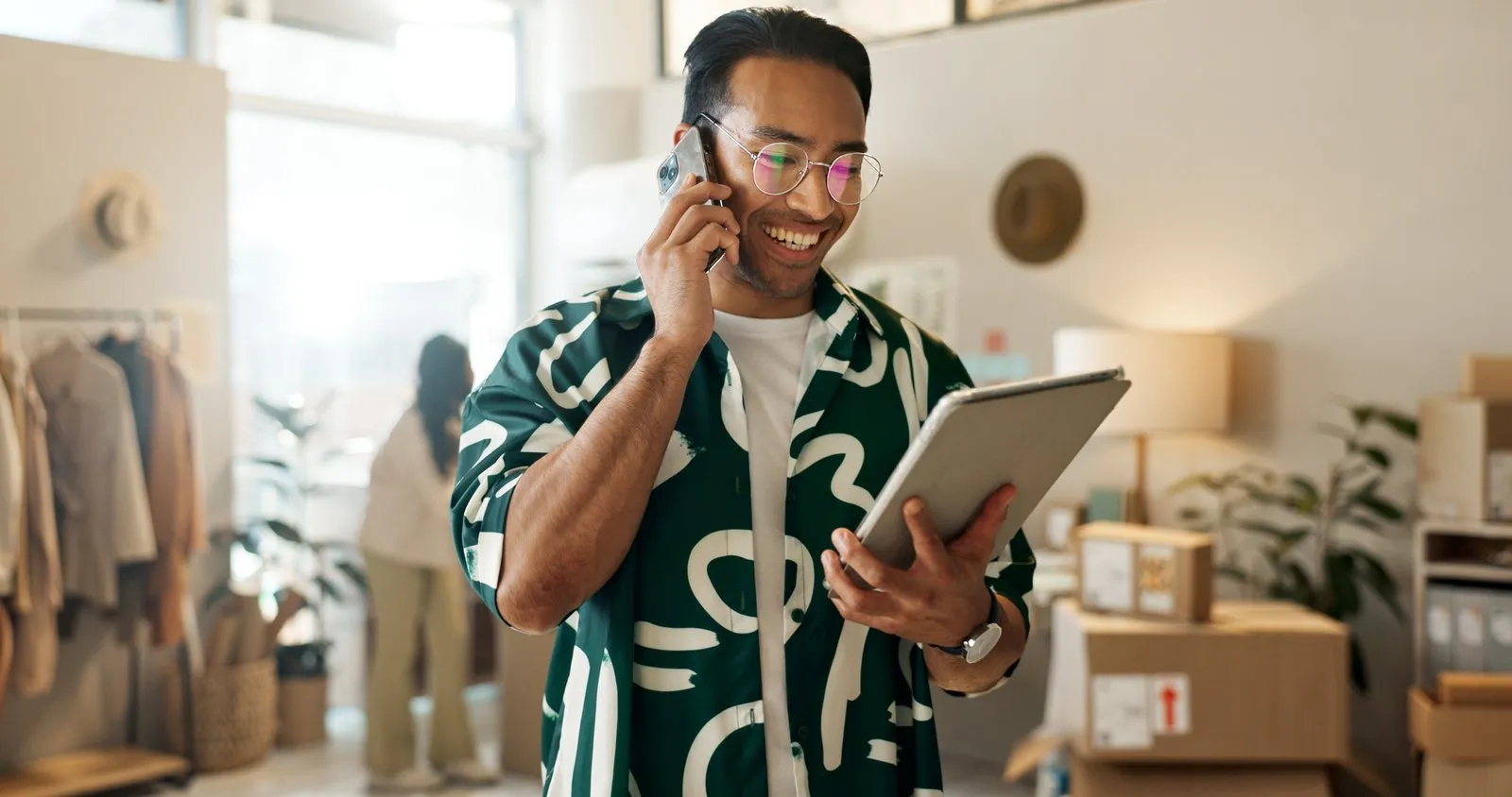 A shop owner on the phone holding a tablet in their store
